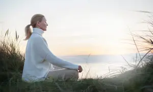 Kobieta w białym swetrze medytuje na plaży, szukając spokoju i sposobu, jak oczyścić umysł.
