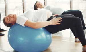 Kobiety w ciąży ćwiczą pilates na dużej, niebieskiej piłce gimnastycznej, dbając o formę i dobre samopoczucie.