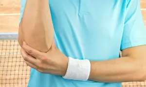Tenisista trzyma się za łokieć, czując ból. Może to być test cozena.