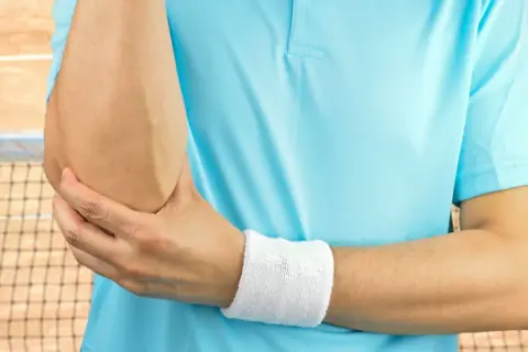 Tenisista trzyma się za łokieć, czując ból. Może to być test cozena.