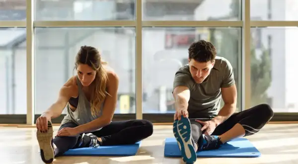 Para ćwiczy stretching, rozciągając nogi na macie. To świetny sposób na poprawę elastyczności.