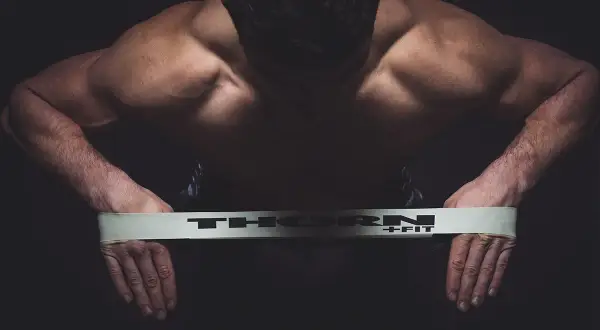 Mięśnie pleców i ramion mężczyzny napinają się podczas ćwiczeń na równowagę z taśmą THORN+FIT.