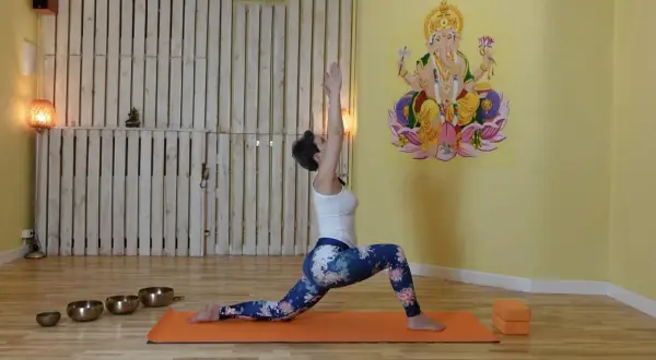Kobieta w pozycji jogi, z rękami uniesionymi do góry, aktywuje czakrę pomarańczową. W tle Ganesha.