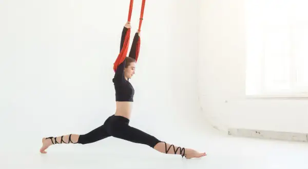 Kobieta wykonuje szpagat w hamaku podczas zajęć air yoga.