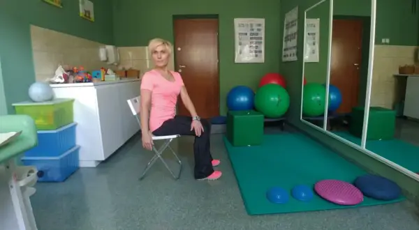 Kobieta wykonuje ćwiczenia na **skręty tułowia** w sali rehabilitacyjnej.