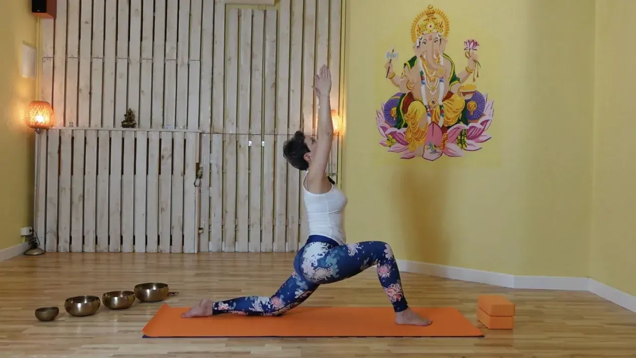 Kobieta w pozycji jogi, z rękami uniesionymi do góry, aktywuje czakrę pomarańczową. W tle Ganesha.
