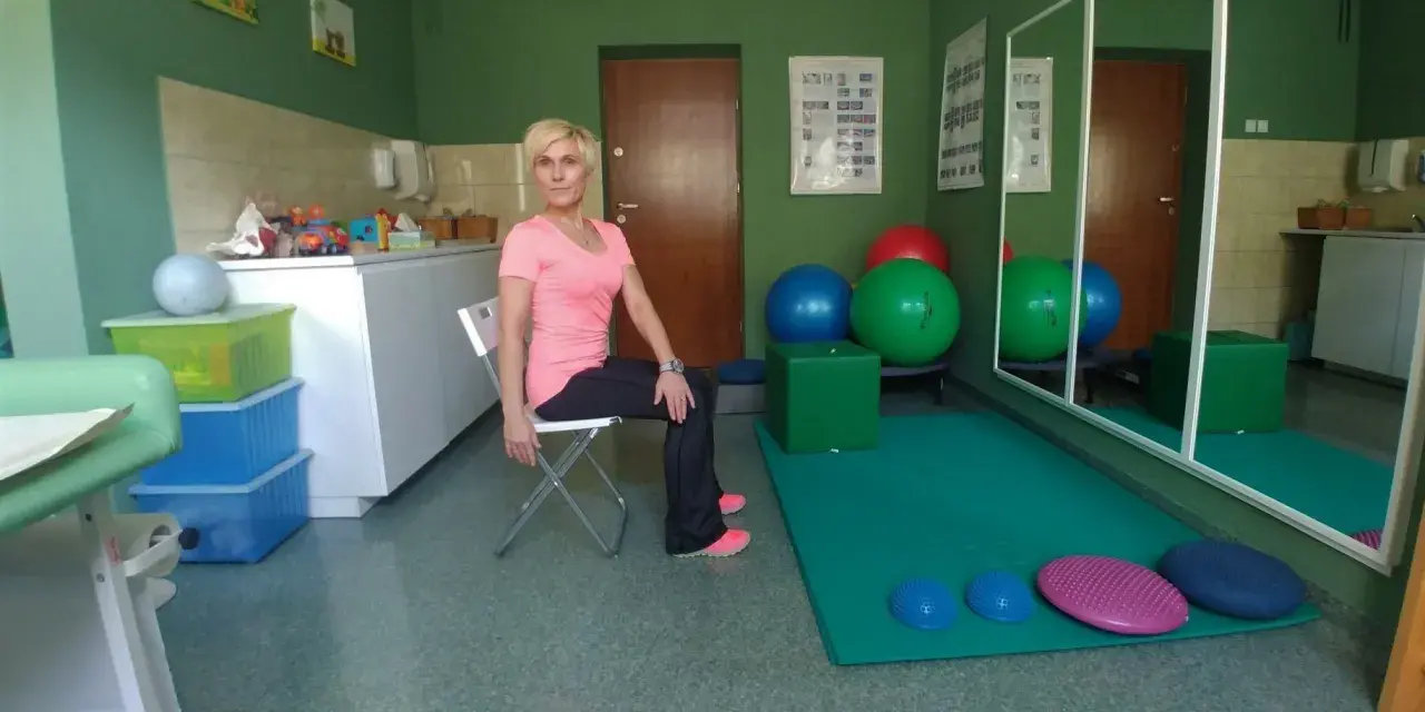 Kobieta wykonuje ćwiczenia na **skręty tułowia** w sali rehabilitacyjnej.