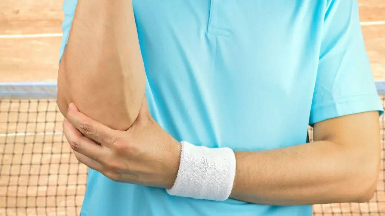 Tenisista trzyma się za łokieć, czując ból. Może to być test cozena.