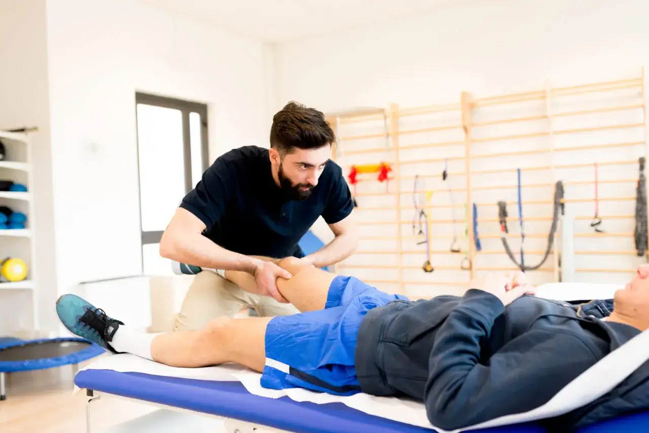 Fizjoterapeuta wykonuje masaż sportowy nogi pacjenta leżącego na kozetce.