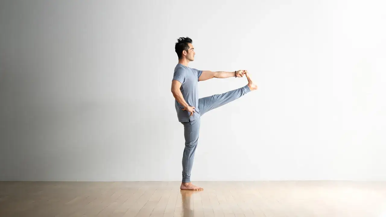 Mężczyzna w pozycji utthita hasta padangusthasana, z uniesioną i chwytaną stopą, ćwiczy równowagę.