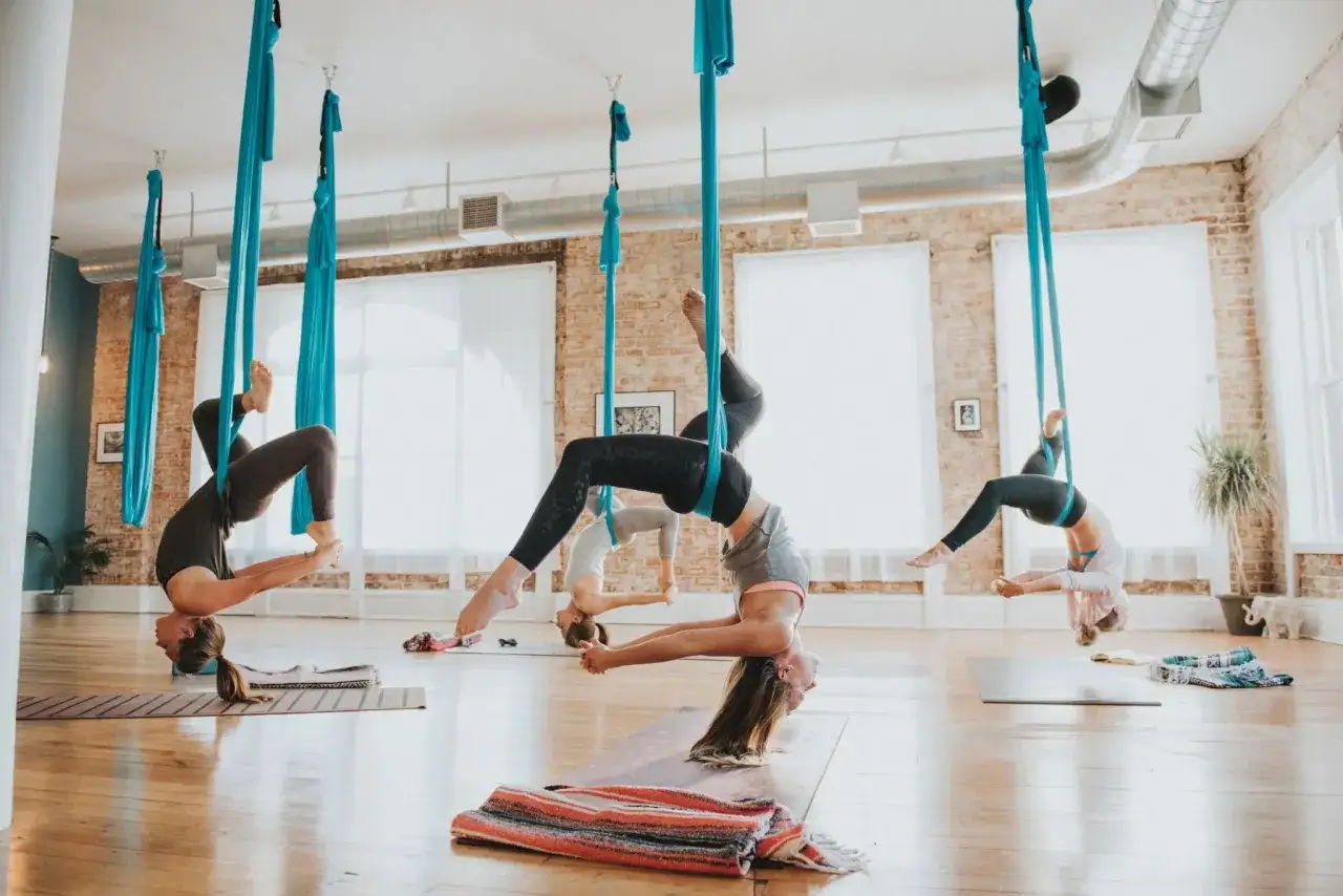 Kobiety ćwiczą air yoga, wisząc w błękitnych hamakach w przestronnej sali.