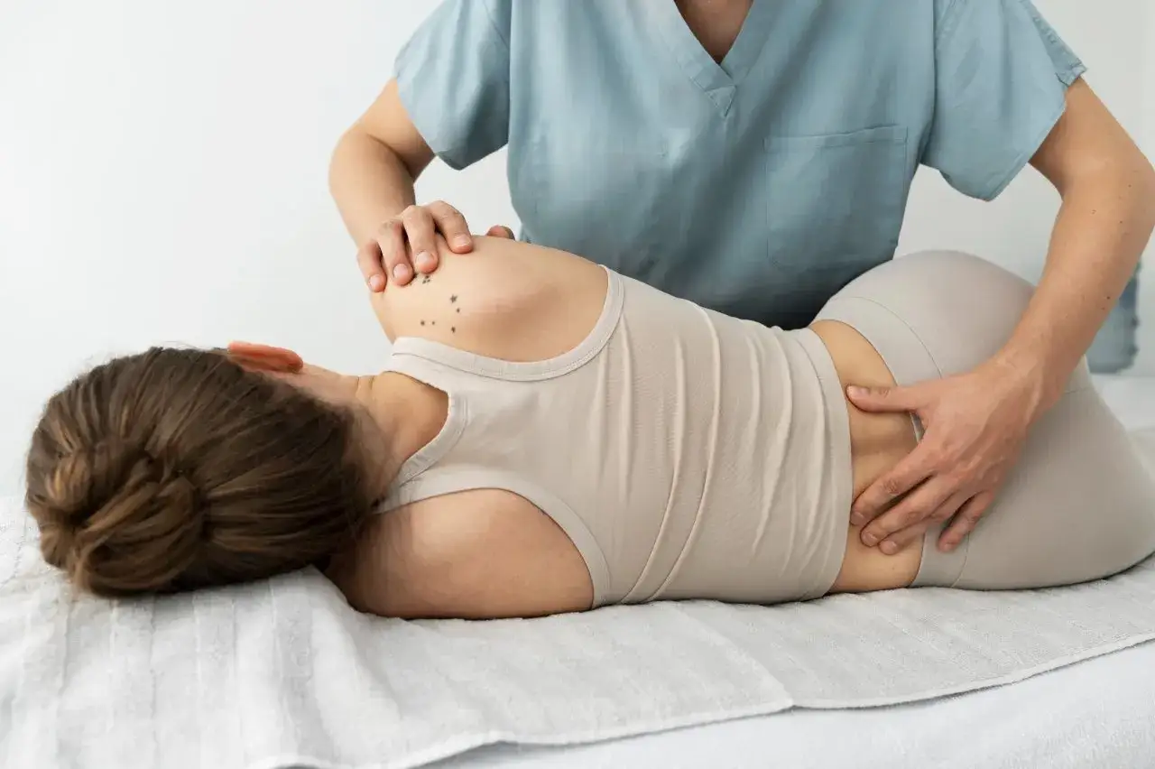 Fizjoterapeuta wykonuje ćwiczenia na rwę kulszową, delikatnie masując dolną część plec&oacute;w pacjentki.