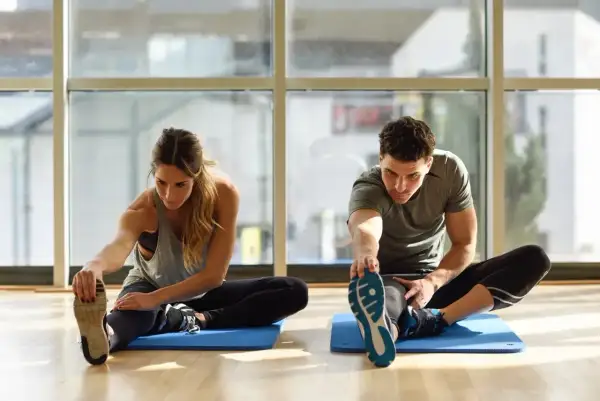 Para ćwiczy stretching, rozciągając nogi na macie. To świetny sposób na poprawę elastyczności.