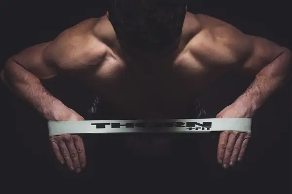 Mięśnie pleców i ramion mężczyzny napinają się podczas ćwiczeń na równowagę z taśmą THORN+FIT.