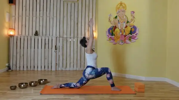 Kobieta w pozycji jogi, z rękami uniesionymi do góry, aktywuje czakrę pomarańczową. W tle Ganesha.