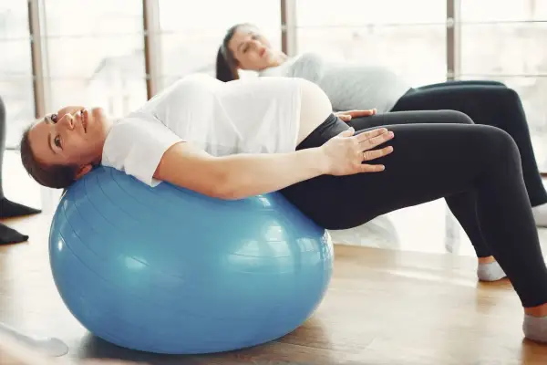 Kobiety w ciąży ćwiczą pilates na dużej, niebieskiej piłce gimnastycznej, dbając o formę i dobre samopoczucie.