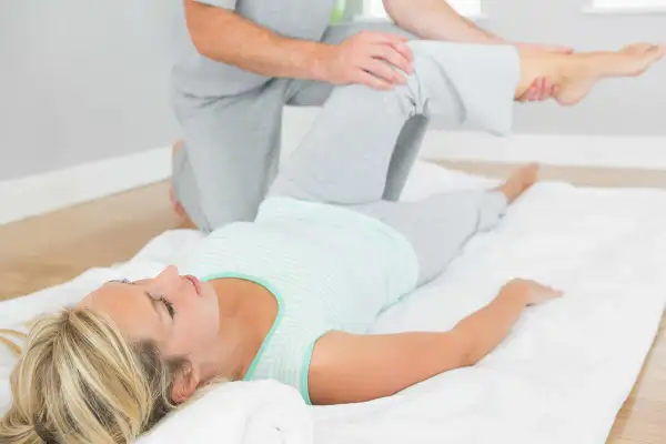 Fizjoterapeuta wykonuje test obera na leżącej kobiecie, sprawdzając ruchomość jej biodra.