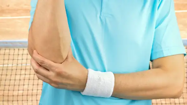Tenisista trzyma się za łokieć, czując ból. Może to być test cozena.